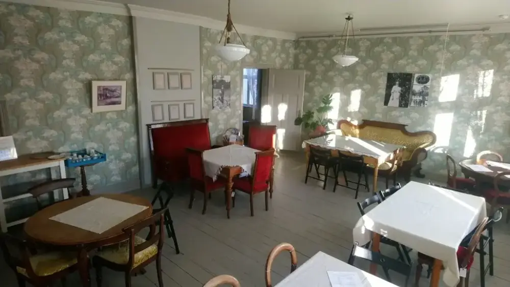 Gammel festsal med eldre møbler i sittegrupper. Blomstrete, lysegrønn tapet.