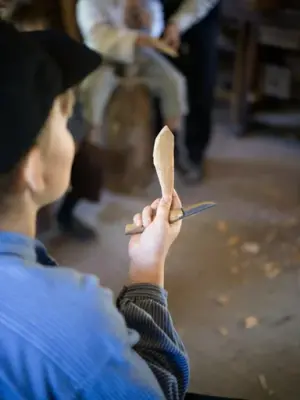 Child holding a carving knife and freshly whittled wooden spoon during an activity at the Carpenter’s Workshop at Norsk Folkemuseum.