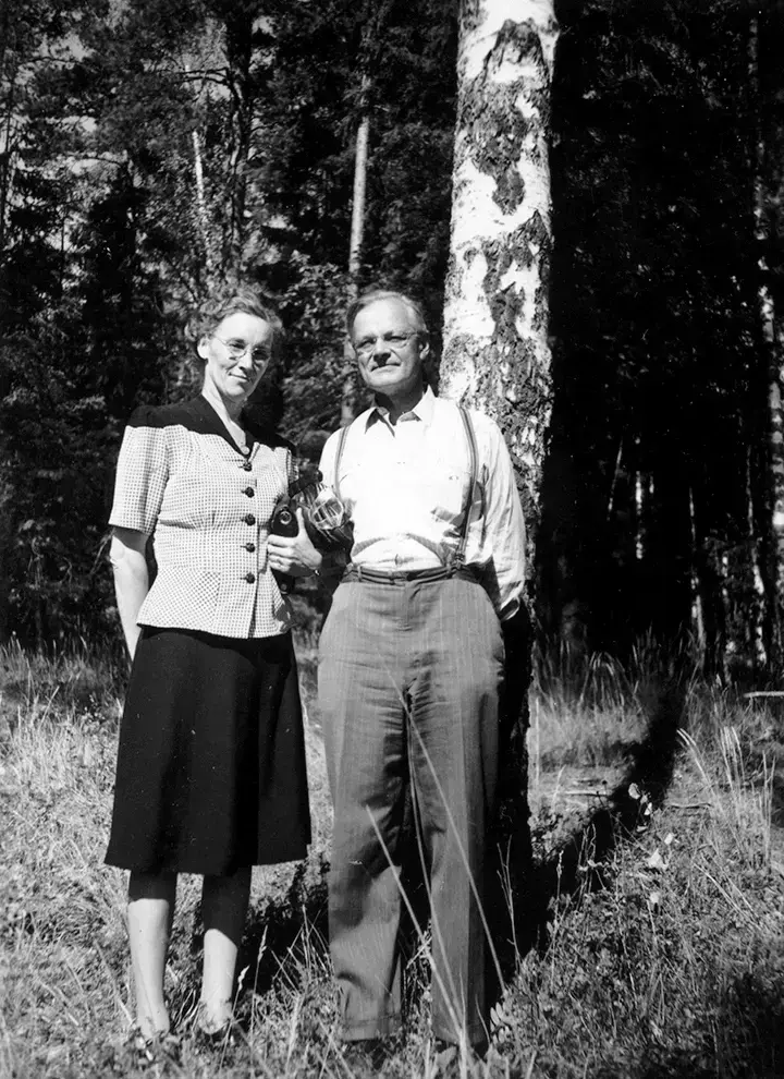 En mann og en kvinne står ved en bjørkestamme. Skog i bakgrunn.