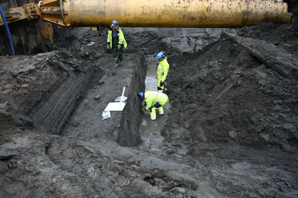 Arkeologisk utgravning ved Alnaelva, hvor lag med elveavsatte gjenstander blir undersøkt. Utgravningen møter utfordringer med både leire og vann som strømmer inn fra flere kilder