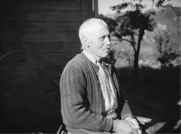 Håkon Hauge sitjande på ein stol framom huset