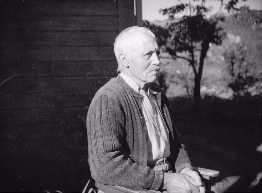 Håkon Hauge sitjande på ein stol framom huset