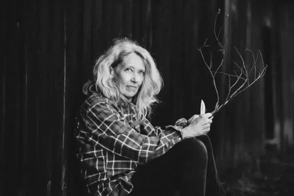 Portrett av Marit O Kaldhol som held i ein spikkekniv og ei grein. 