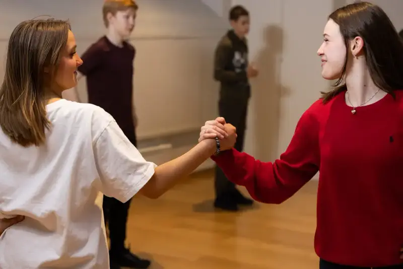 To ungdommer holder hverandre i hendene og smiler under øvelse i norsk folkedans.