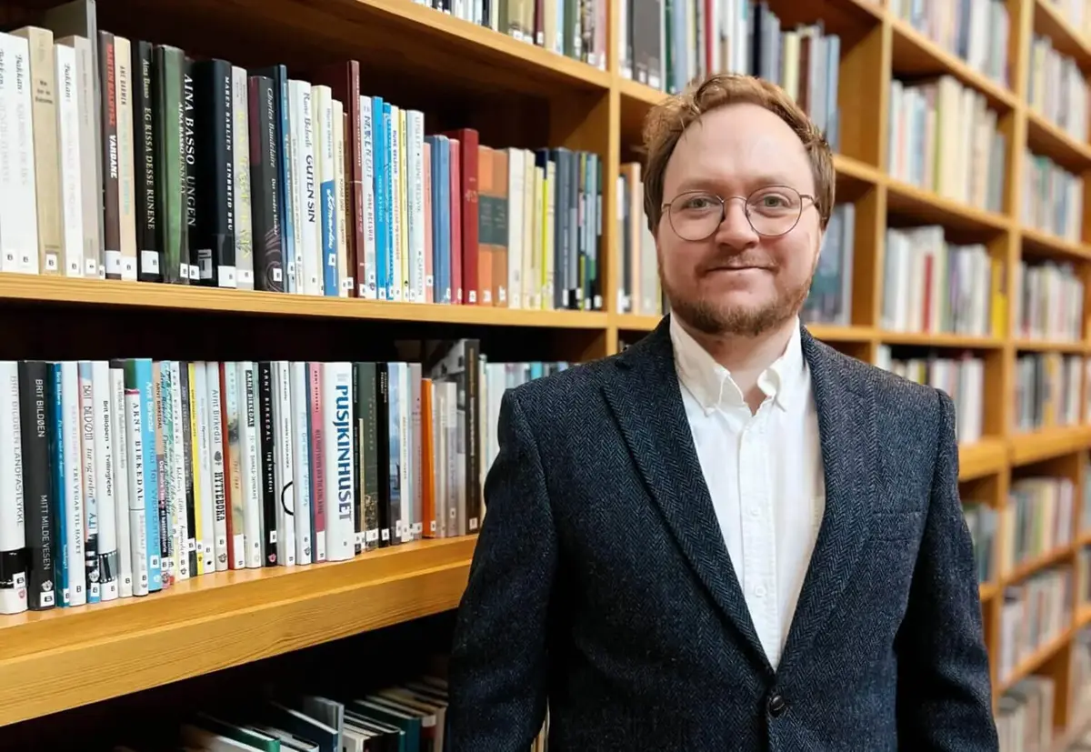 Olav Øyehaug Opsvik smiler mot kamera med bokhylle som bakgrunn.