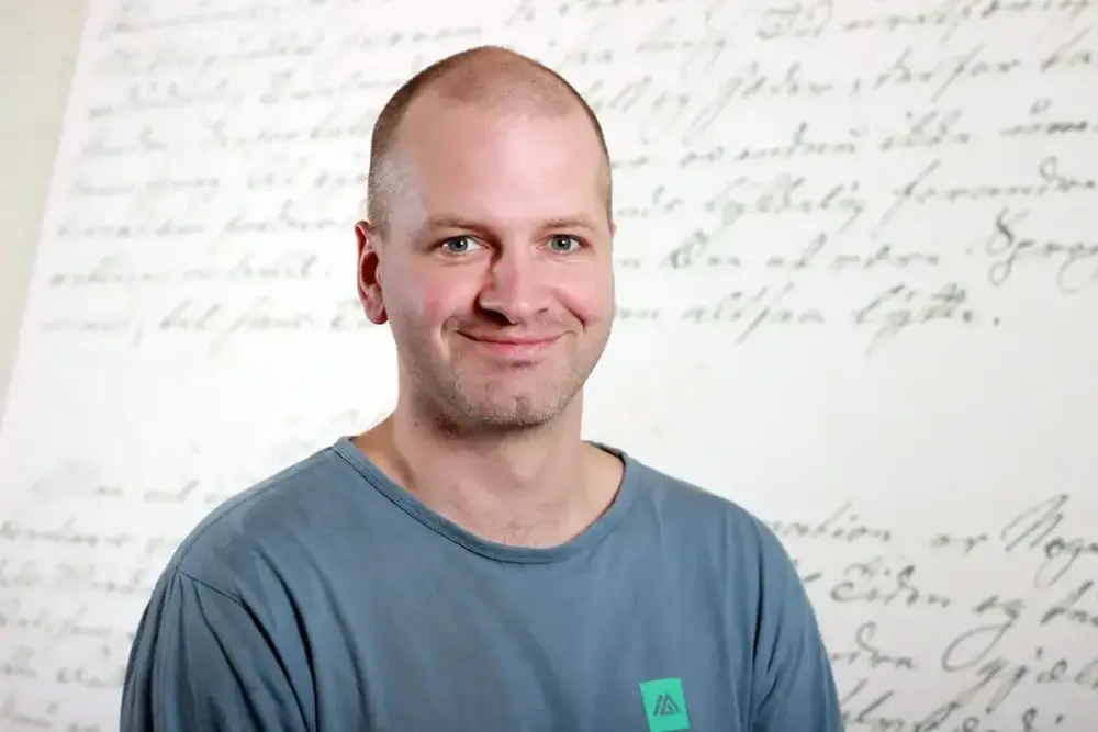 Portrettfoto av Stein Arnold Hevrøy framom ein skriftvegg i utstillinga i Aasentunet