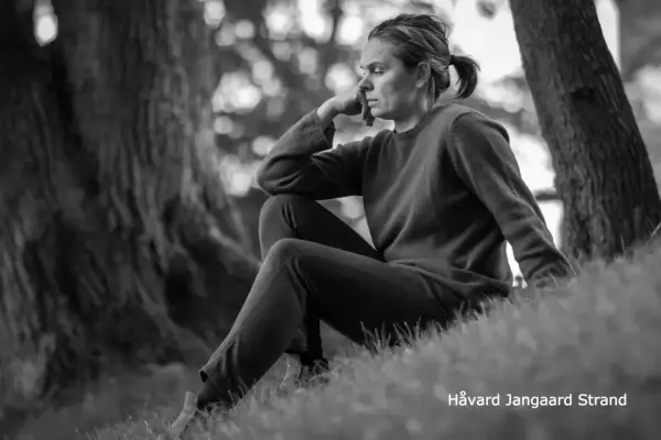 Portrettfoto av Inger Bakke sittande i graset med tre i bakgrunnen