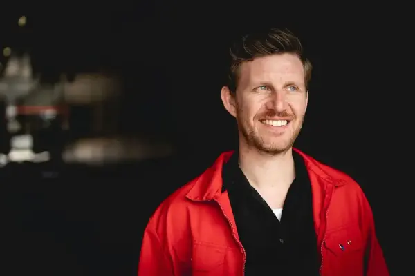 Portrettfoto av Jens Kihl med raud jakke og mørk bakgrunn