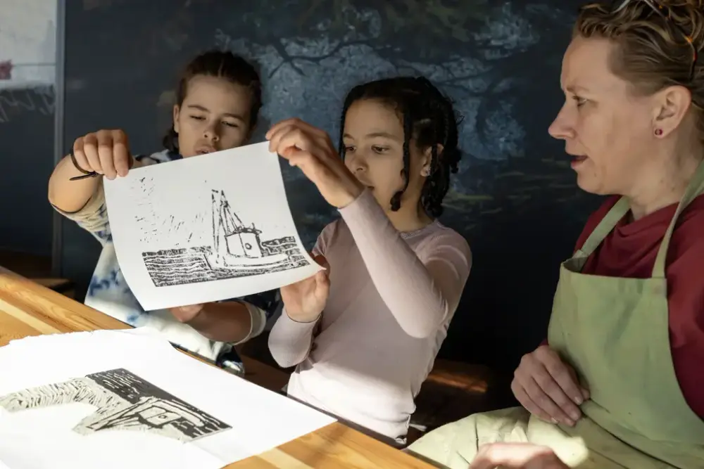 To barn viser frem et grafisk trykk av en båt under et grafikkverksted.