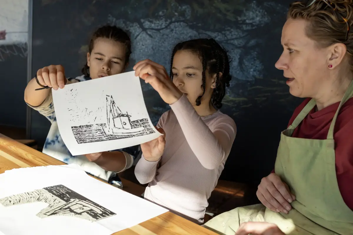 To barn viser frem et grafisk trykk av en båt under et grafikkverksted.