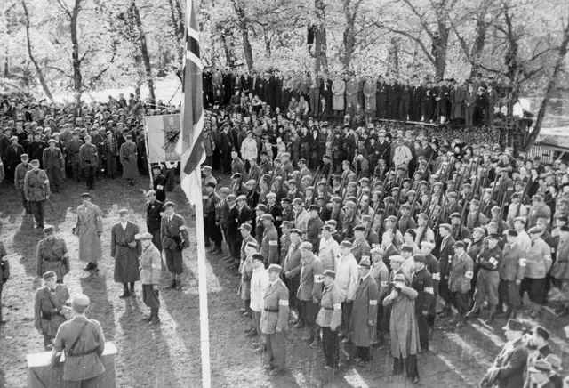 Parade for avsnittssjef Bertel B. Hensmoen ved Eidsvollsbygningen 17. mai 1945, med hjemmefrontsoldater og publikum samlet.