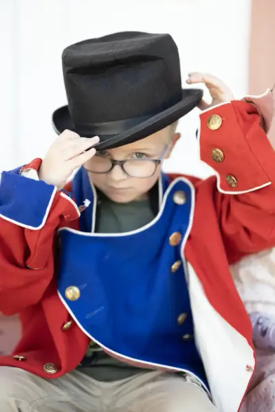 Barn i utkledningsklær inspirert av 1800-talls mote, med rød og blå uniform og høy hatt, under et formidlingstilbud ved Eidsvoll 1814.