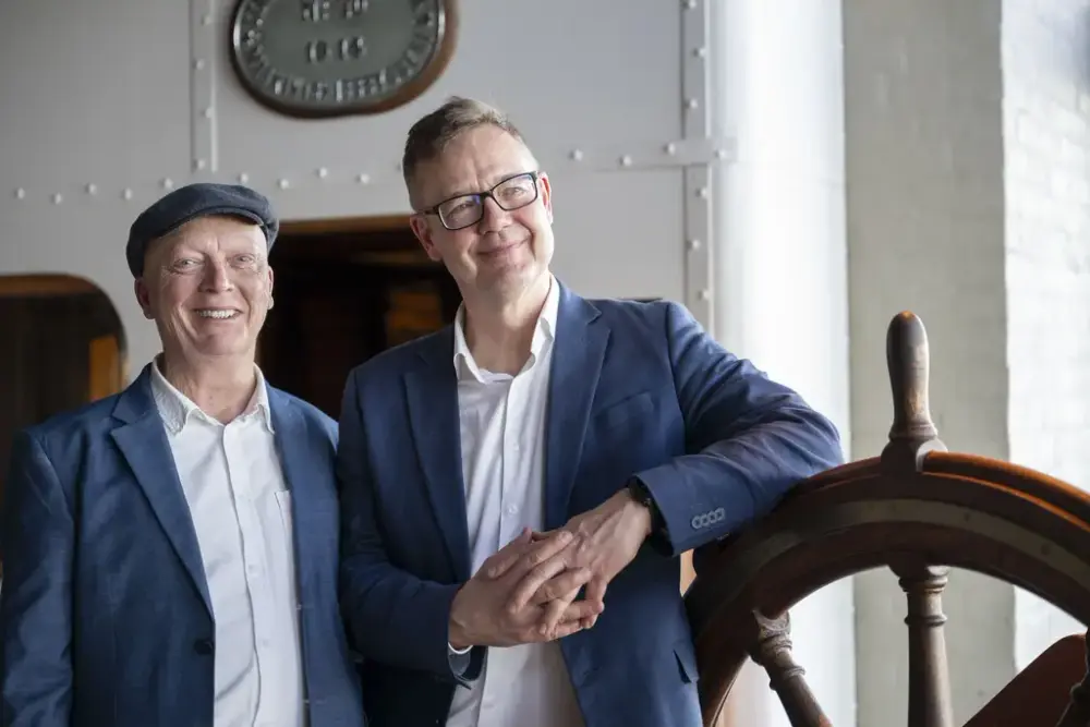Art collector Matthew Goodheart and Chief Curator Eyvind Bagle stand by a ship’s wheel at the Norwegian Maritime Museum.