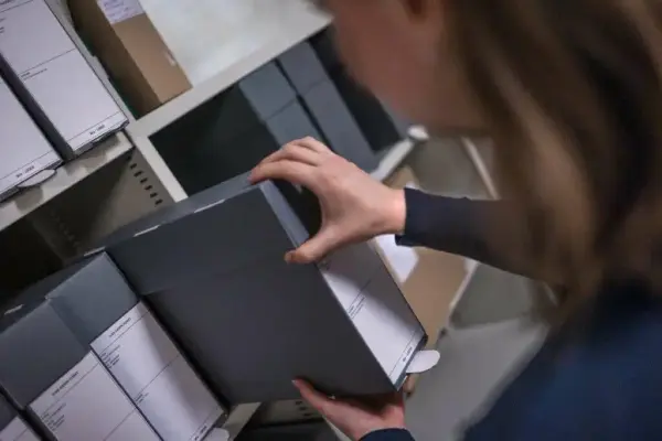 ein person tek ut ei boks frå ei arkivhylle