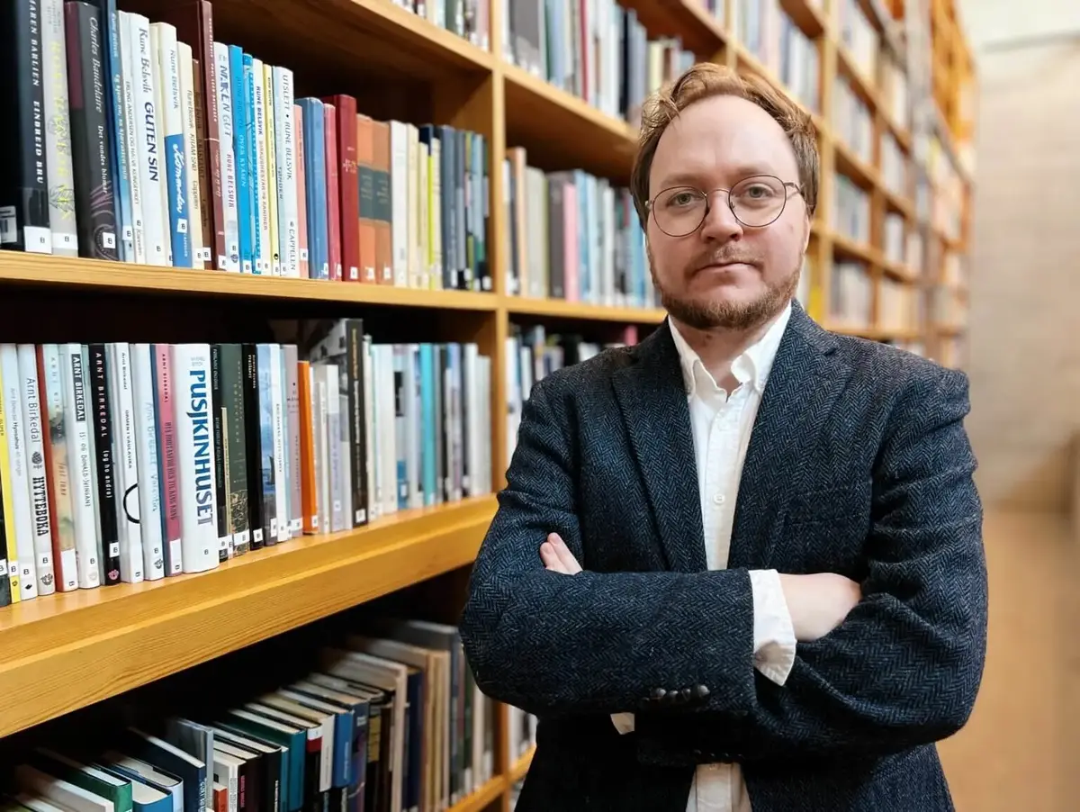Portrett av ein alvorleg Olav Øyehaug Opsvik med armane i kors ved bokhylla i biblioteket i Aasentunet