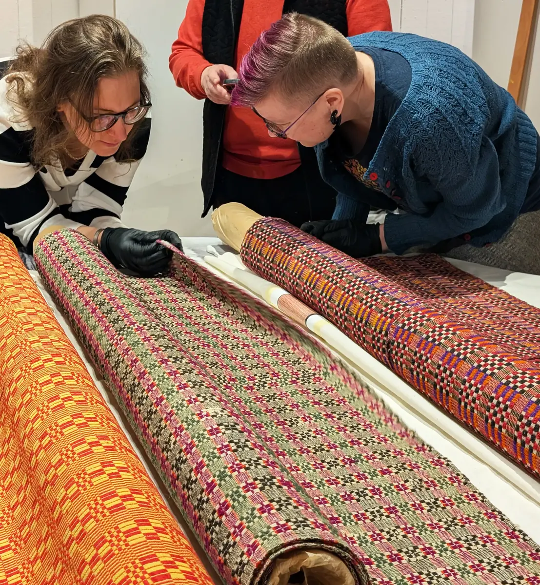 två personer undersöker en väv