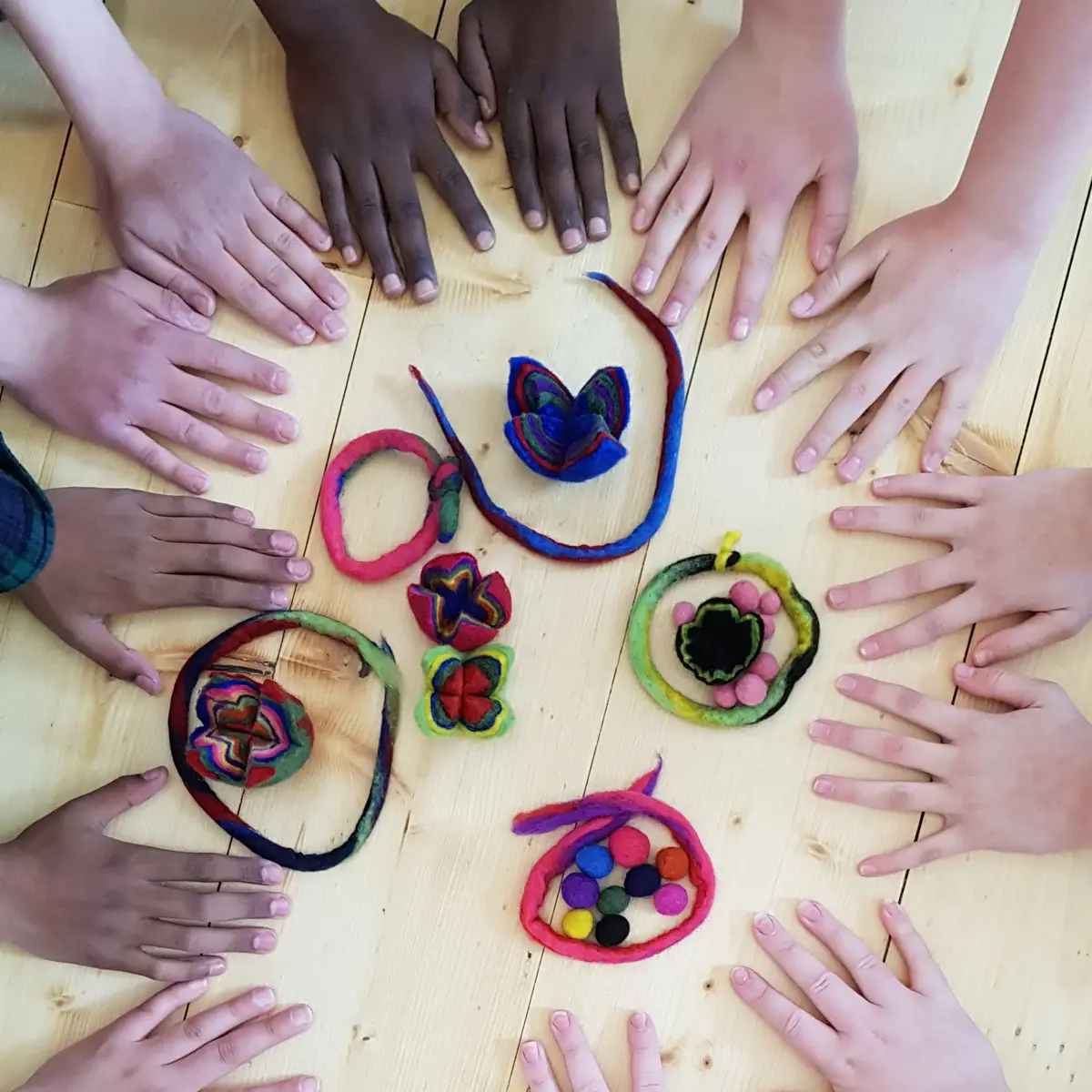 flera barnhänder placerade i cirkel runt tovade föremål 
