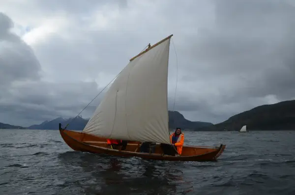 tradisjonsbåt i tre under seil, to mennesker i båten