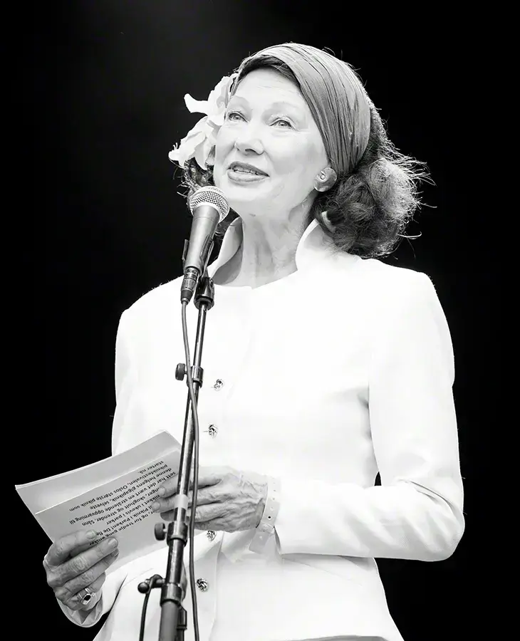 Åse Kleveland i kvit jakke står bak ein mikrofon