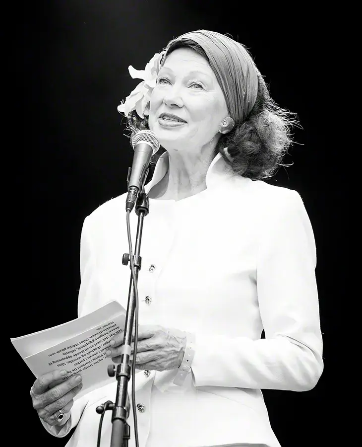 Åse Kleveland i kvit jakke står bak ein mikrofon