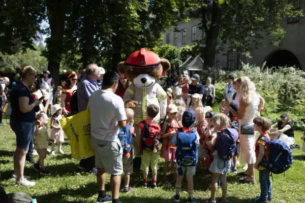 Brannbamsen Bjørnis hilser på barn ute i friluftsmuseet til amcar- og brannbilhelg på Norsk Folkemuseum.