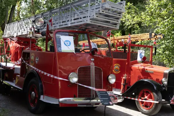 To røde veteranbrannbiler med stigeløftere og norske flagg utstilt på Norsk Folkemuseum under amcar- og brannbilhelg.