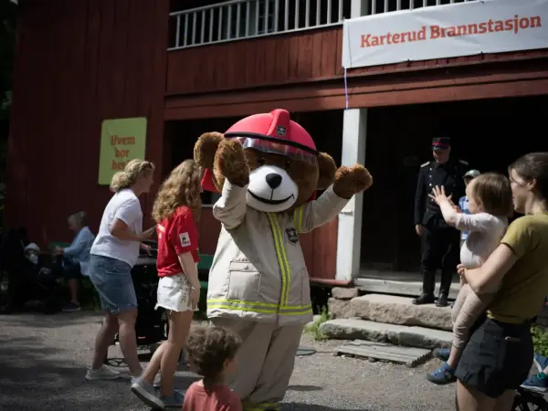 Brannbamsen Bjørnis hilser på barn og voksne utenfor Karterud Brannstasjon under amcar- og brannbilhelg på Norsk Folkemuseum.