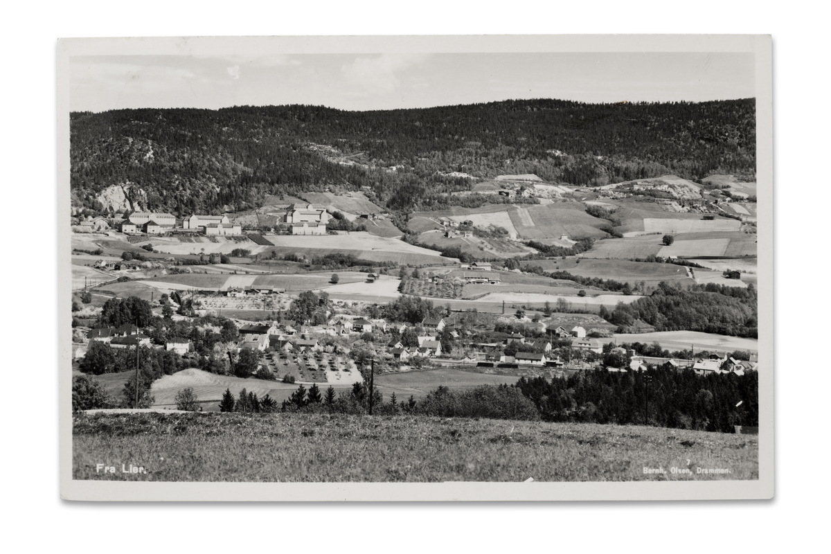 Lierbyen sett mot øst med Lier Asyls bygninger i bakgrunnen. Bildet er tatt midt i 1930-årene. I midtre, venstre del stikker taket på Lier Meieri opp. På skrå ned mot høyre for meieriet ligger Hegsbro med «Askgården» (mørk fasade) nedenfor. Til høyre for den, ser vi Lier Hotels ruvende bygning. Langt mot høyre, Hegg skoles karakteristiske bygning.