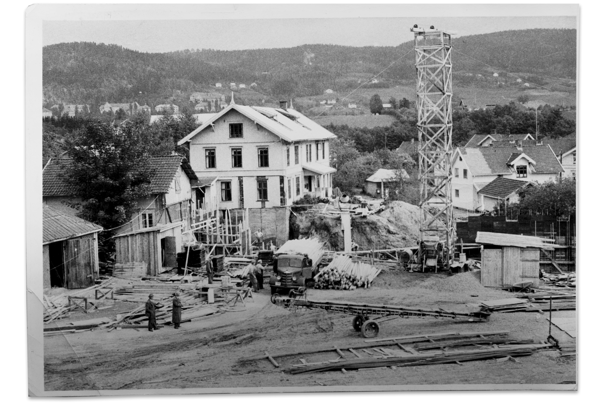 Tomta klargjøres for å gi plass til rådhusets første byggetrinn ca. 1955. Midt i bildet er Hegsbro lett gjenkjennelig, til høyre Dåsen, Christian Muggeruds hus. Planleggingen av det nye administrasjonsbygget startet i 1953. Arkitektene la fram to forslag for kommunestyret. Det ene var å bygge ved Haugestad, det andre i tilknytning til Hegsbro. Bygningen ble tatt i bruk i januar 1957.