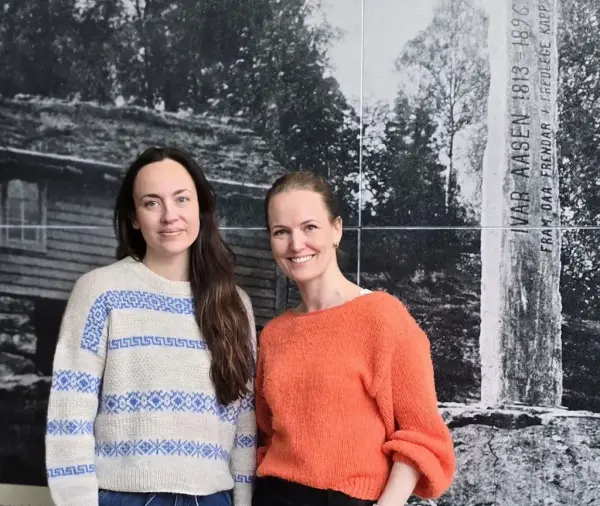 Ida Aarflot Kornberg og Kjersti Perjord Vartdal framom eit bilde av bautaen i Aasentunet
