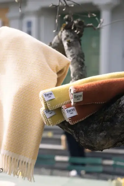 Wool blankets in warm colors from Røros Tweed hanging on a tree branch outside the museum shop at Norsk Folkemuseum.