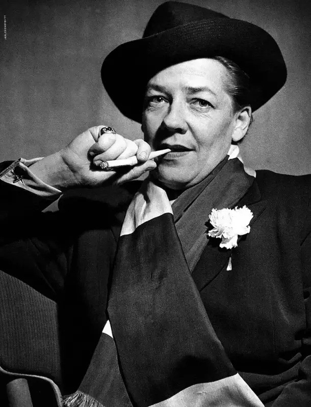 Ett svartvitt porträttfoto på Kai Gullmar. Hon har hatt och kavaj, en blomma i kavajens knapphål och en scarf. I handen håller hon en cigarr. 