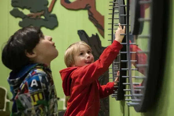 Närbild på två barn i Småfolk som snurrar på hjul som sitter på väggarna