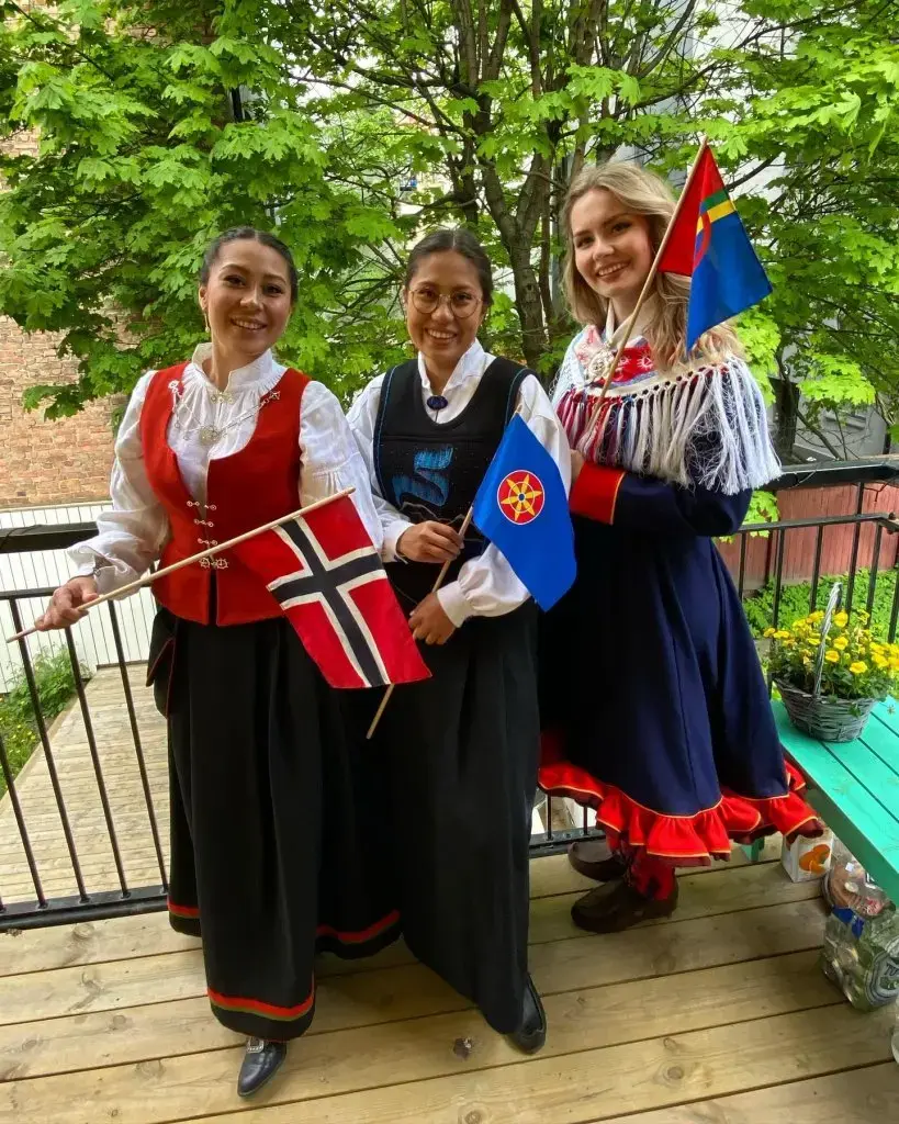 tre jenter i bunad med norsk, kvensk og samisk flagg