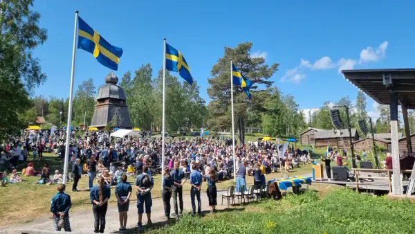 Tre flaggstänger med svenska flaggan, uppradade scouter och publik i bakgrunden.