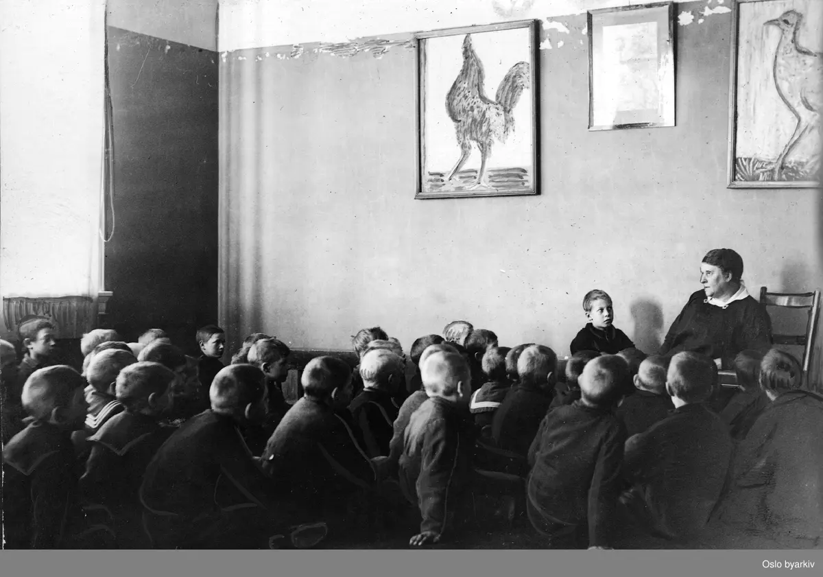 "Lærer og forfatterinnen Regine Normann forteller eventyr for ""sine gutter"". Eventyrstund med Regine Normann i Blåsalen på Deichmanske bibliotek. ..Albumtittel: ""Sofienberg skole femti år - første september 1933."""