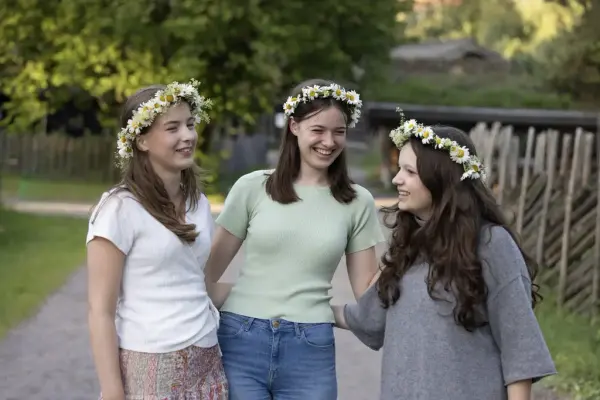 Three young women wearing flower crowns smiling and enjoying the Midsummer Festival at Norsk Folkemuseum.