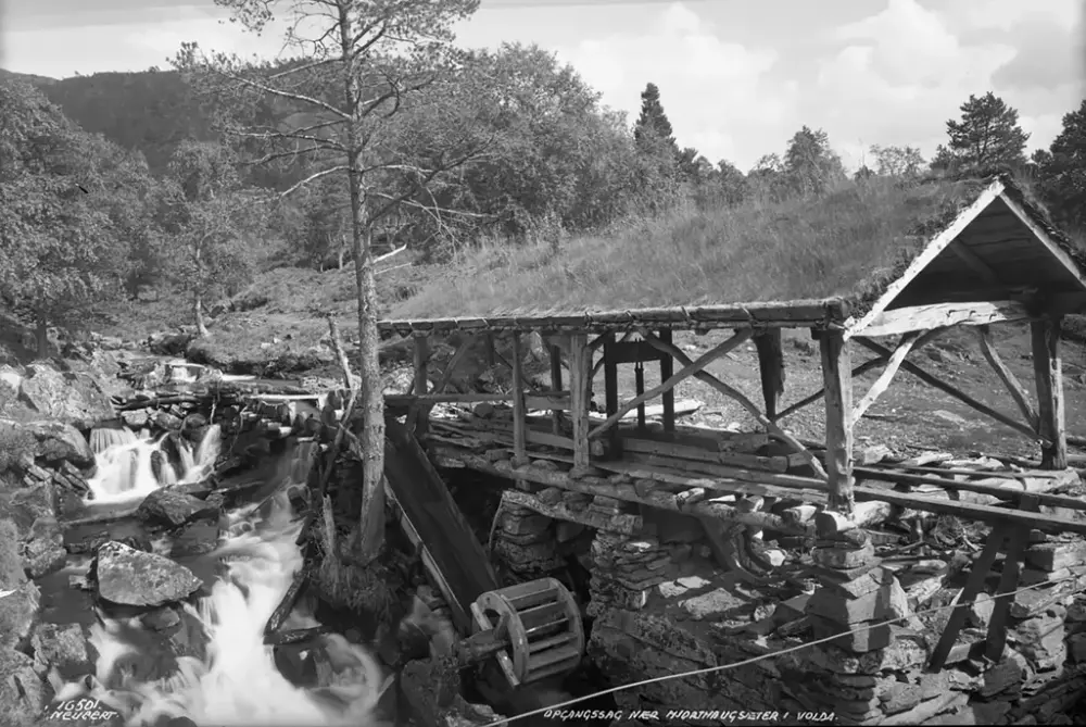 Historisk foto av en vassdrevet oppgangssag ved elv i skogkledd landskap.