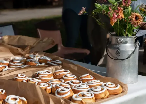 Flere brett med kanaleboller med melisglasur. En vase med blomster ved siden av. 