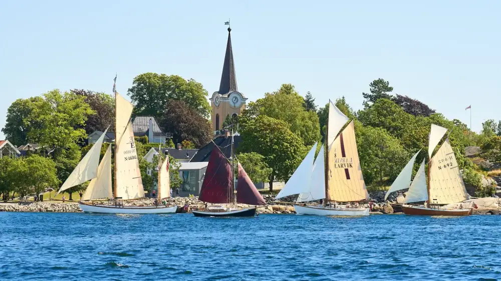 Viser fire seilende seilbåter med Tollerodden, grønne trær og Larvik kirke i bakgrunn.
