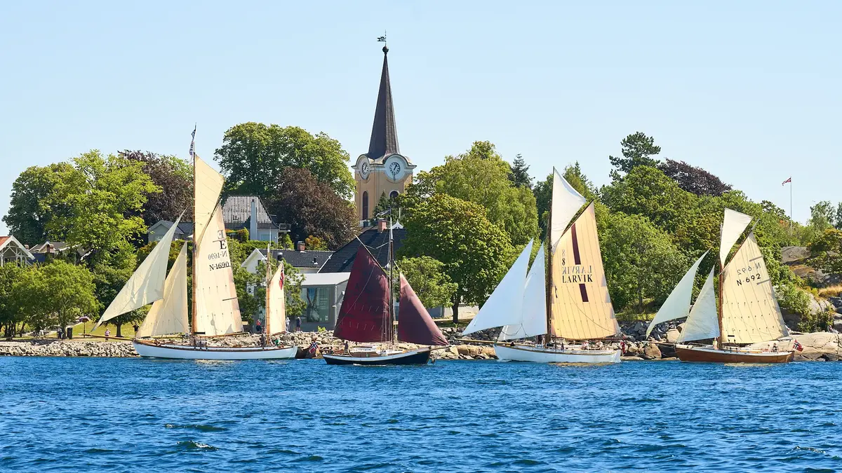 Viser fire seilende seilbåter med Tollerodden, grønne trær og Larvik kirke i bakgrunn.