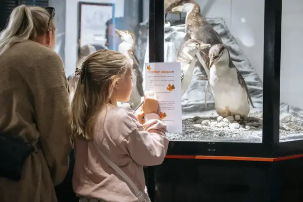 En mor og datter svarer på en rebus i den biologiske utstillingen, her med de utstoppede pingvinene.