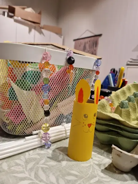 På bordet i studion. En gul påskhare av en toarulle, äggkartoinger och pärlor i olika färger. 