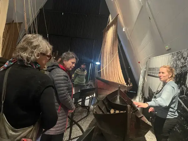 Museumsformidler forteller om en tradisjonsbåt til tre voksne besøkende i Båthallen på Norsk Maritimt Museum.