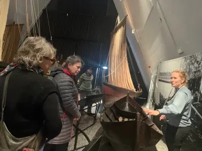 Museumsformidler forteller om en tradisjonsbåt til tre voksne besøkende i Båthallen på Norsk Maritimt Museum.