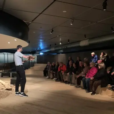Museumsformidler snakker til en gruppe voksne besøkende om vikingtidens båtbyggeri på Norsk Maritimt Museum.