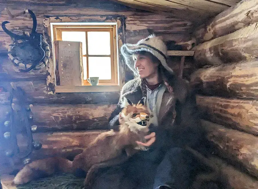 Kvinna med hatt och räv i knät, sitter i en timmerkoja