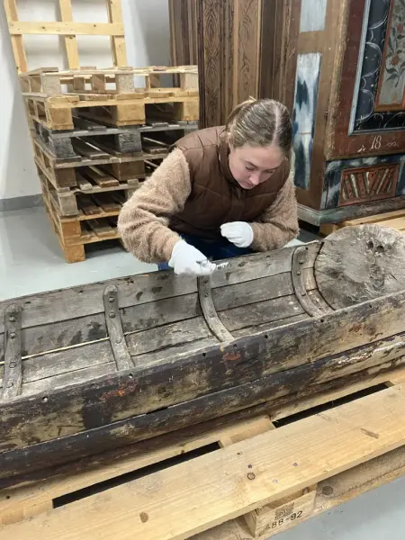 En kvinna sitter hukad över en ackja i trä och tar prover. 