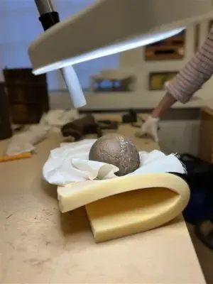 En kanonkula på en bit skumgummi som ligger på ett bord. En lampa lyser upp kanonkulan. I bakgrunden står en person. 