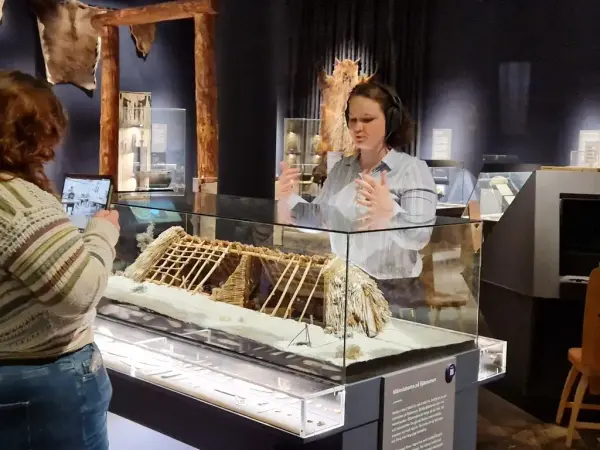 En guide står i en utställning och filmas av en annan kollega på en surfplatta. 